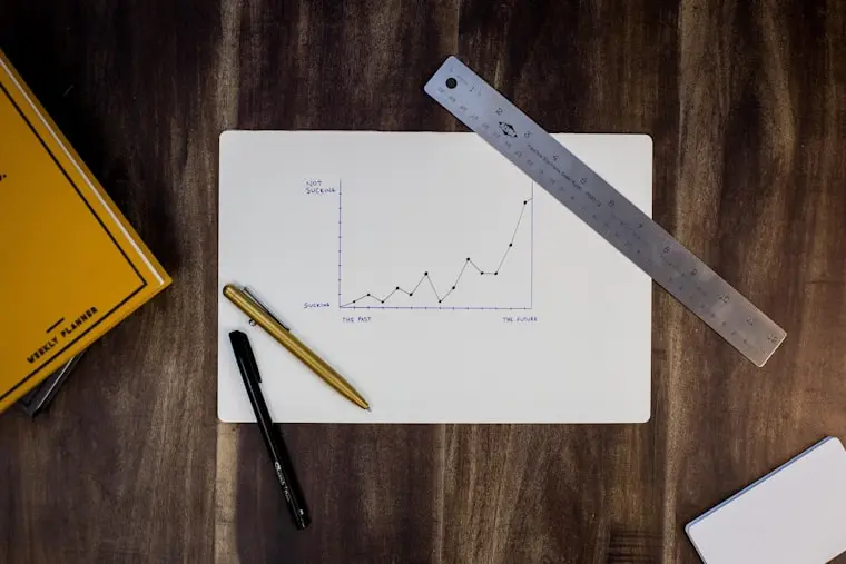 A hand-drawn line graph on white paper showcasing upward growth trends alongside a ruler, weekly planner, and pens, representing a digital marketing strategy execution.